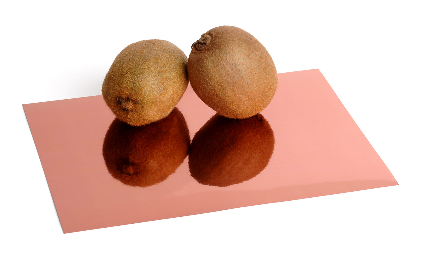 Copper foil board with a reflective, mirrored finish. Two kiwis sit atop the sheet and are reflected in its surface.