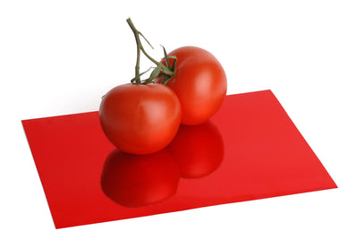 Red foil board with a reflective, mirrored finish. Two tomatoes sit atop the foil board and are reflected in its surface.